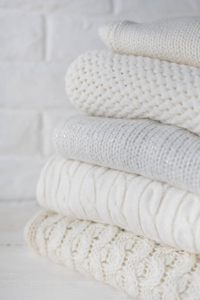 Stack of white cozy knitted sweaters and beads against the background of white brick wall. - Valokuva, kuva