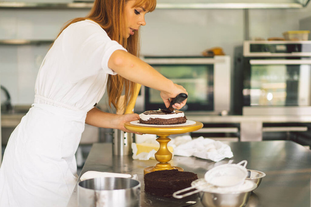 Chica pastelera está preparando una galleta de pastel con crema blanca y chocolate. Pasteles de cocina. - Foto, Imagen