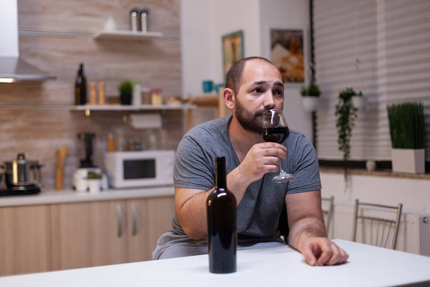 Kaukázusi férfi kezében üveg bor ül a konyhában - Fotó, kép