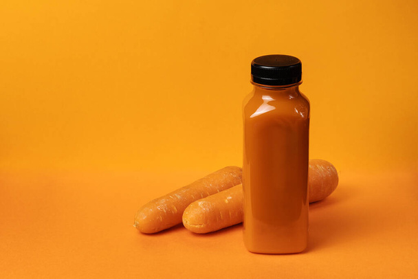A bottle of carrot juice and two carrots aside on an orange background with copy space - Photo, Image