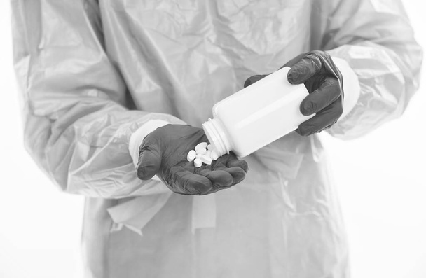 doctor epidemiologist hold vitamin pills jar in hand wearing safety protective costume during creating vaccine from coronavirus pandemic outbreak, covid 19 treatment - Foto, imagen
