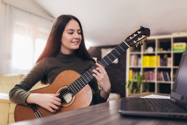 Girl playing guitar with computer, learn to play with an online course - Photo, Image