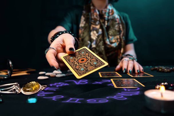 Fortune-telling on cards. The fortune teller hands over a Tarot card. The zodiac circle surrounds on the table. The concept of divination, astrology and esotericism. - Photo, image