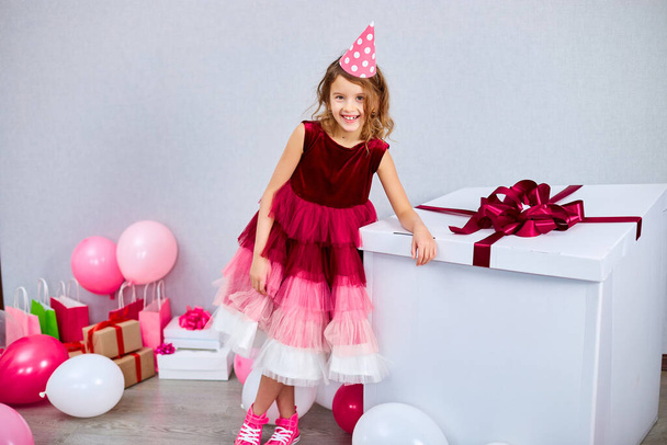 ピンクのドレスとスニーカーの楽しい女の子は、大きなプレゼントボックス、自宅の誕生日パーティーストリーマーでの風船、ハッピー誕生日。お祝い - 写真・画像
