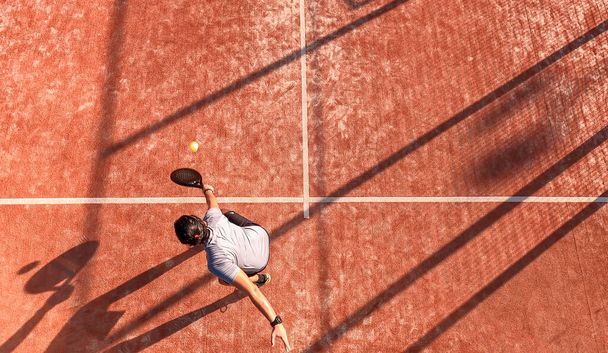 Vista superior de um jogador de tênis de remo que está batendo a bola com a raquete em um campo ao ar livre. Ele está posicionado perto da linha. - Foto, Imagem