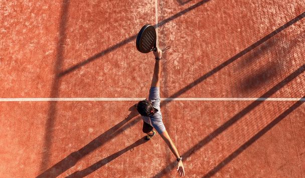 Uitzicht van bovenaf van een man die paddle tennis speelt en net de bal heeft geraakt op een buitenbaan. - Foto, afbeelding