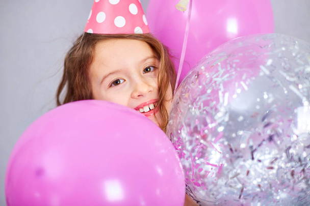 Portrait de mignonne, joyeuse petite fille en robe rose et chapeau jouer avec des ballons à la maison fête d'anniversaire banderoles, Joyeux anniversaire. Célébration - Photo, image