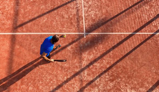 Κάτοψη ενός επαγγελματία παίκτη τένις κουπί dribbling την μπάλα και εξυπηρετούν σε ένα υπαίθριο γήπεδο κέντρο αθλητισμού. - Φωτογραφία, εικόνα
