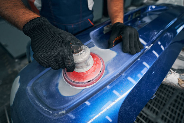 Mechanic using grinding unit on blue bumper - Фото, изображение