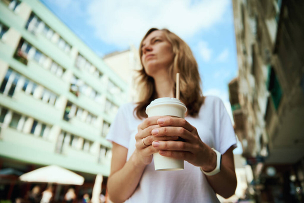 Koffie papieren beker in vrouwenhanden. Vrouw drinkt koffie om naar de straat te gaan. - Foto, afbeelding
