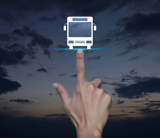 Hand pressing bus flat icon over sunset sky, Business transportation service concept - 写真・画像