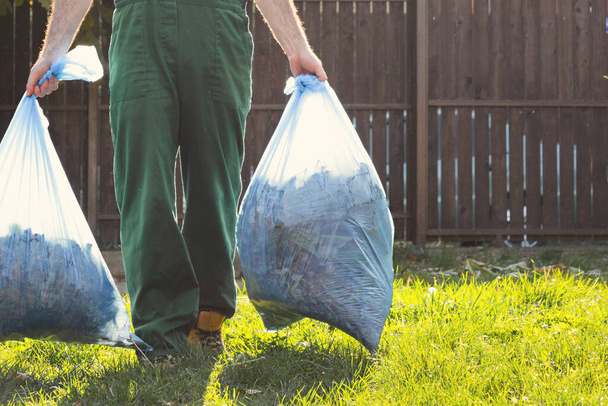 Der Gärtner entfernt die Säcke mit Kompost. Licht. Grüne Uniform. Nahaufnahme. - Foto, Bild