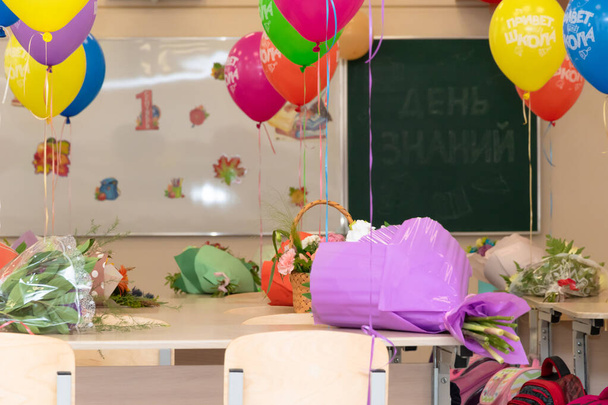 Schulstunde am 1. September ohne Schüler mit bunten Luftballons und Blumen auf Tischen vor dem Hintergrund der Schultafel. Die Inschriften lauten Wissenstag und Hallo Schule. Nahaufnahme - Foto, Bild