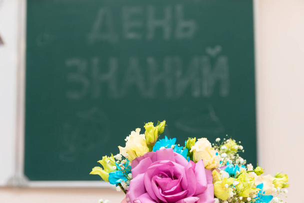 Ένα μπουκέτο όμορφα φωτεινά λουλούδια σε ένα γραφείο του σχολείου την 1η Σεπτεμβρίου. Η επιγραφή στο σχολικό συμβούλιο είναι η Ημέρα της Γνώσης. Επιλεκτική εστίαση. Κοντινό πλάνο - Φωτογραφία, εικόνα