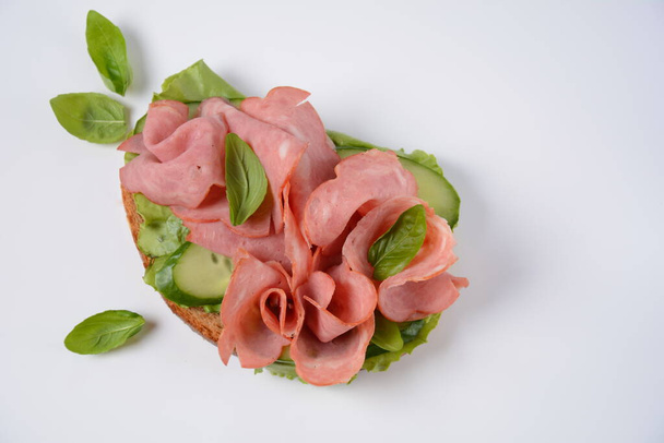 Open ham Sandwich with cucumbers, basil, and a crusty slice of rye bread and salami - Foto, afbeelding