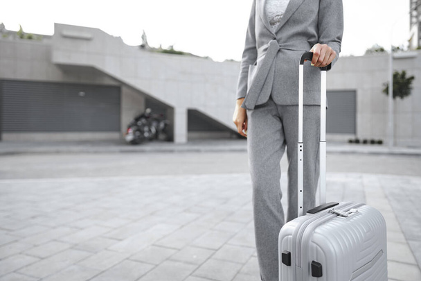 Businesswoman in gray suit on business trip walking with her luggage in the city - Foto, afbeelding