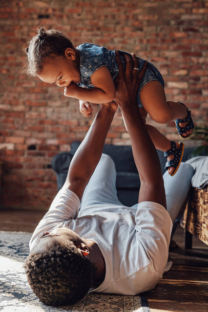 Amante padre sosteniendo a su hija acostada en el suelo dentro de la habitación - Foto, imagen