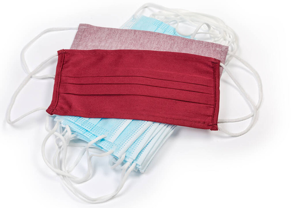 Dark red and pale red textile protective face masks lie on a stack of the light blue disposable medical masks on a white backgroun - Photo, Image