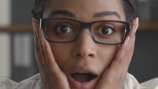 Unglaublicher Erfolg. Überraschte Afroamerikanerin mit Brille berührt staunend ihre Wangen und blickt in die Kamera - Filmmaterial, Video
