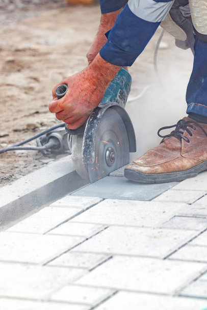 A builder's hands tensely cut paving slabs with a grinder and a diamond saw in a cloud of cement dust during the day. Close-up. Vertical image, copy space. - Photo, image
