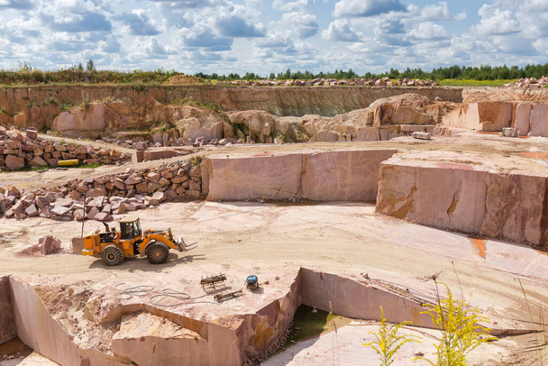 Part of operating quarry for the extraction of red granite and quarry forklift loader in him at summer day - Photo, Image