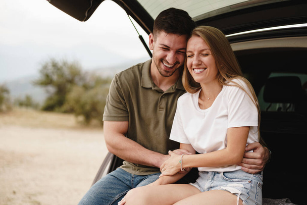 Young happy couple on a road trip sitting in car trunk - Photo, Image
