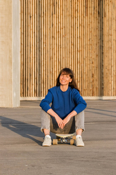 Giovane donna seduta su uno skateboard nel parco. - Foto, immagini