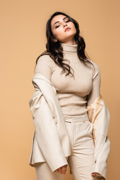 young model in turtleneck and blazer posing isolated on beige - Foto, afbeelding