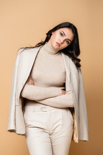 young model in turtleneck and blazer posing with crossed arms isolated on beige - Photo, Image