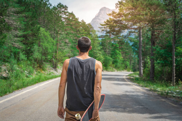 Young hipster holding a cool longboard in his hand. Beautiful concept of travel. Millennial journey of adventure. Skateboard skating ride. Sports in wild nature. - Foto, Imagem