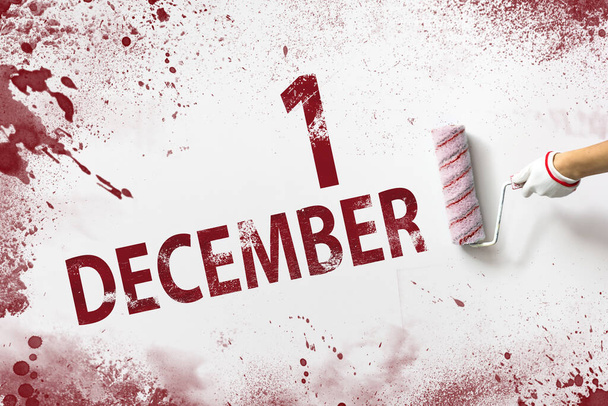 1 de diciembre. Día 1 del mes, fecha del calendario. La mano sostiene un rodillo con pintura roja y escribe una fecha de calendario sobre un fondo blanco. Mes de invierno, concepto del día del año - Foto, imagen