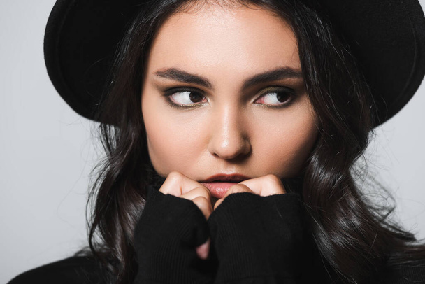 close up of brunette woman in black fedora hat and turtleneck looking away isolated on grey - Foto, afbeelding