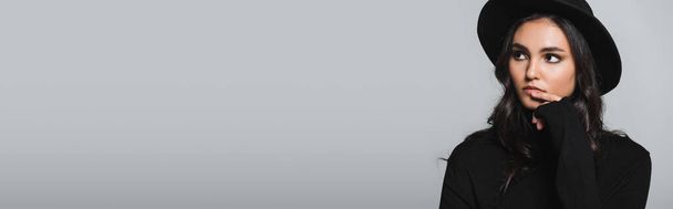 мечтательный молодой модели в черной шляпе Fedora и водолазка глядя вдали изолированы на серый, баннер - Фото, изображение