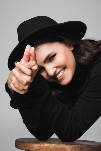 young happy woman in fedora hat showing finger gun gesture isolated on grey - Foto, Imagem