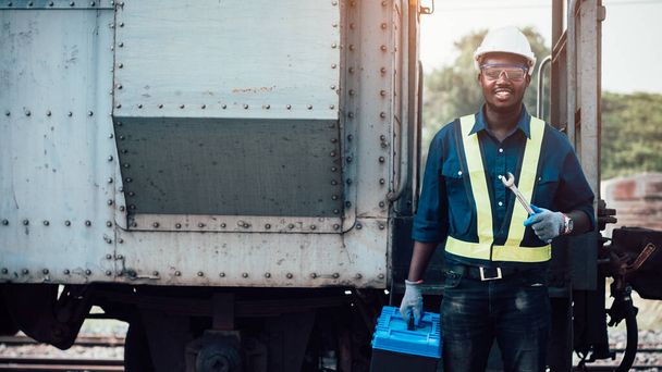 Técnico africano ingeniero de máquinas con un casco, arboledas y chaleco de seguridad está utilizando una llave inglesa para reparar el tren - Foto, imagen
