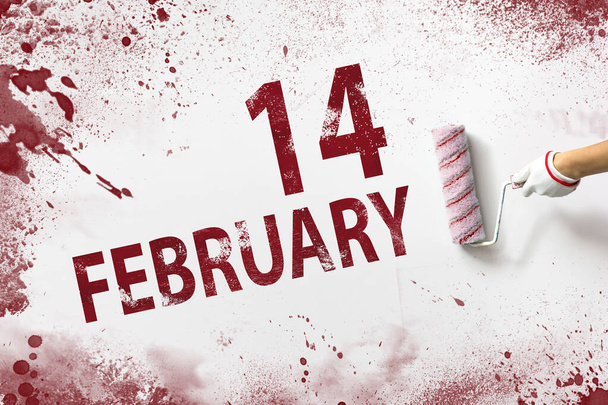 14 februari. Dag 14 van de maand, kalenderdatum. De hand houdt een rol met rode verf vast en schrijft een kalenderdatum op een witte achtergrond. Winter maand, dag van het jaar concept - Foto, afbeelding