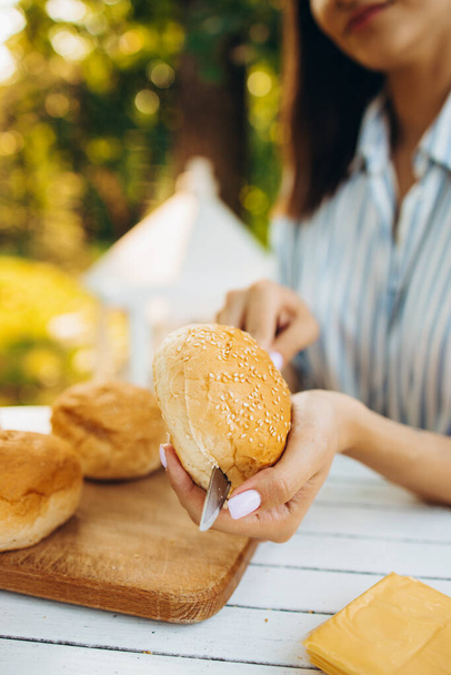 Image recadrée de fille coupant des pains hamburgers pour pique-niquer manger sur la chaude journée d'été à l'extérieur - Photo, image