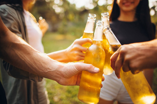 Cropped image of beer bottles clinking. Friends summer day gathering. Cheers - 写真・画像