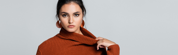 young woman adjusting knitted sweater and looking at camera isolated on grey, banner - Foto, immagini