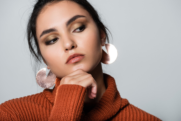 young woman in warm sweater and earrings looking away isolated on grey  - Foto, Imagen