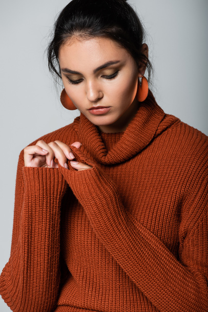 young woman in earrings and knitted sweater looking down isolated on grey - Photo, Image
