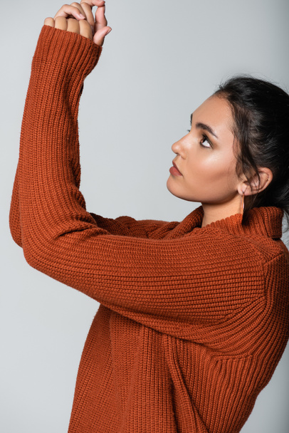 young woman in earring and knitted sweater looking up isolated on grey - Photo, Image