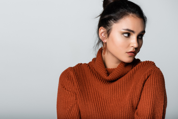 pretty young woman in earrings and knitted sweater looking away isolated on grey - Photo, Image