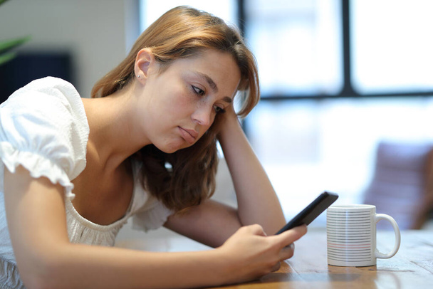 Frustrated and bored woman using smart phone checking content sitting at home - Photo, Image