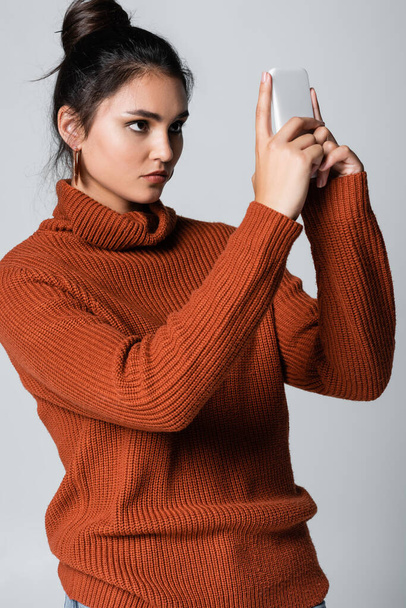 young woman in knitted sweater using smartphone isolated on grey - Foto, immagini