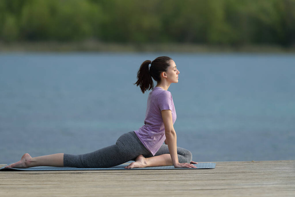Visão lateral retrato de corpo inteiro de uma mulher fazendo pose de ioga em um cais de lagoa - Foto, Imagem