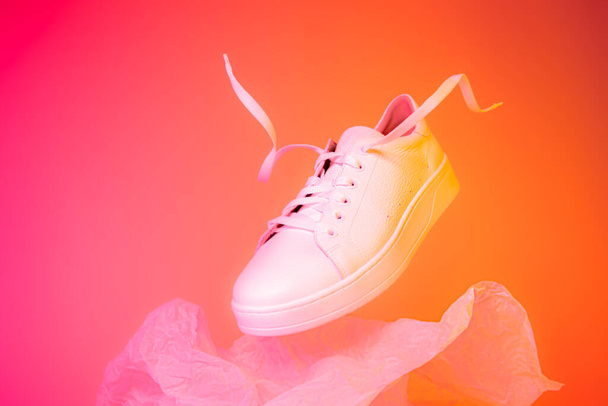 Fashion - white leather sneakers shoe. Footwear levitating on the bright pink and orange background. Layout with free copy (text) space. - Fotografie, Obrázek