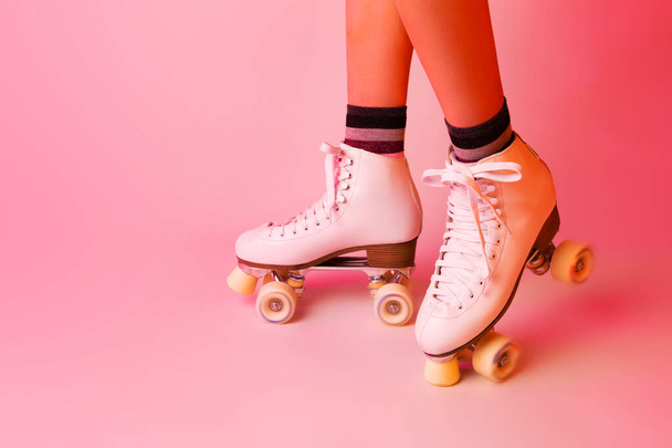 Sports equipment and recreation - classic white leather roller skates and girls legs. Pastel pink background. Layout with free copy space. - Zdjęcie, obraz