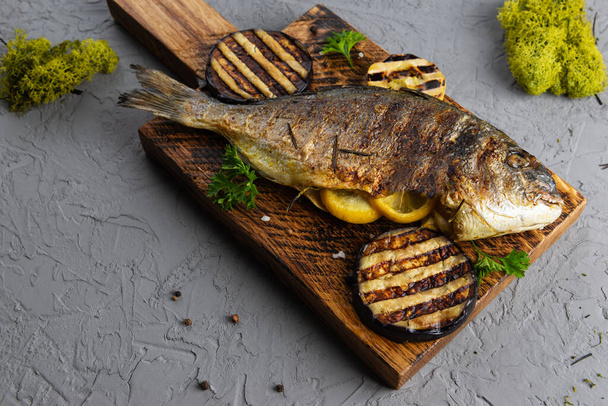 Grillezett töltött dorádó hal citrommal, fűszerekkel és padlizsánnal, fa táblán. - Fotó, kép