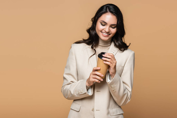 happy young woman in trendy suit holding paper cup isolated on beige - Foto, Imagem